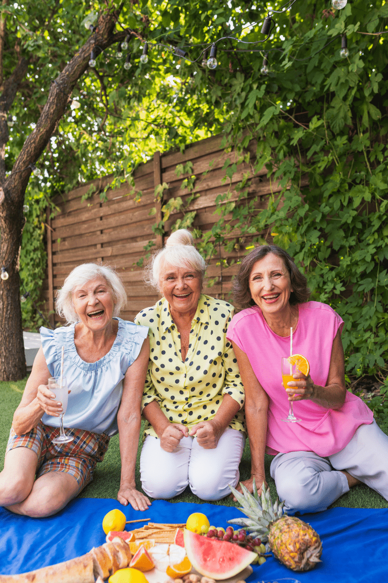 A photograph of three older women smiling and holding drinks outdoors.