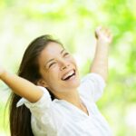 Woman with her arms spread looking upwards towards a sunny sky