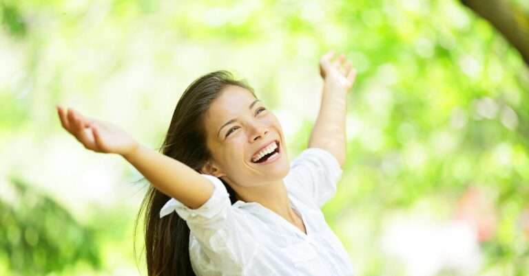 Woman with her arms spread looking upwards towards a sunny sky