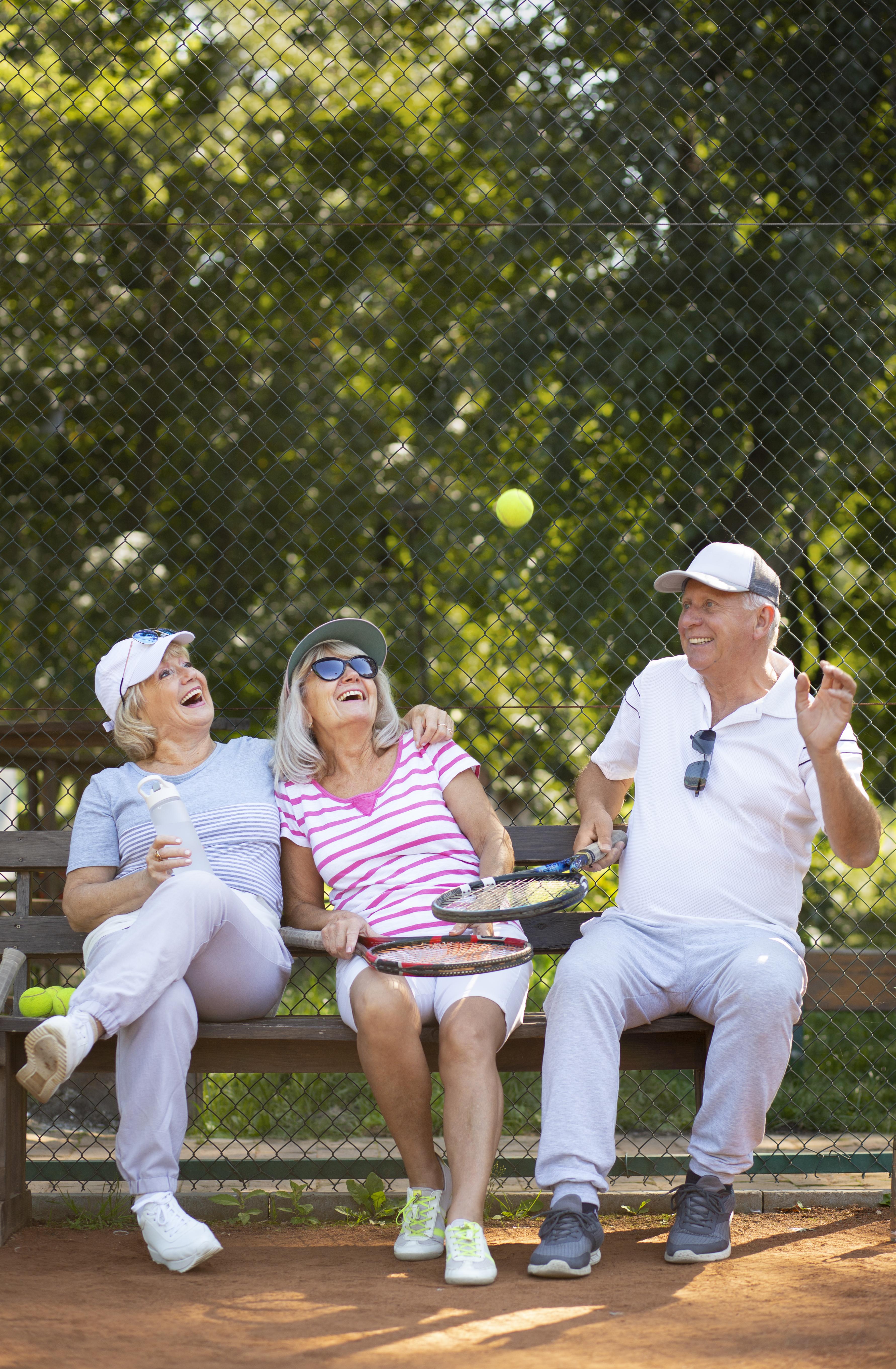 full shot happy friends sitting bench in tennis clothes