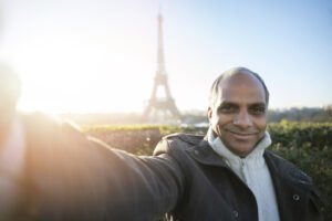 An older man taking a selfie on vacation with the Eifel tower in the background.