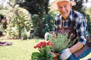 Older adult smiling while holding a planter with flowers.